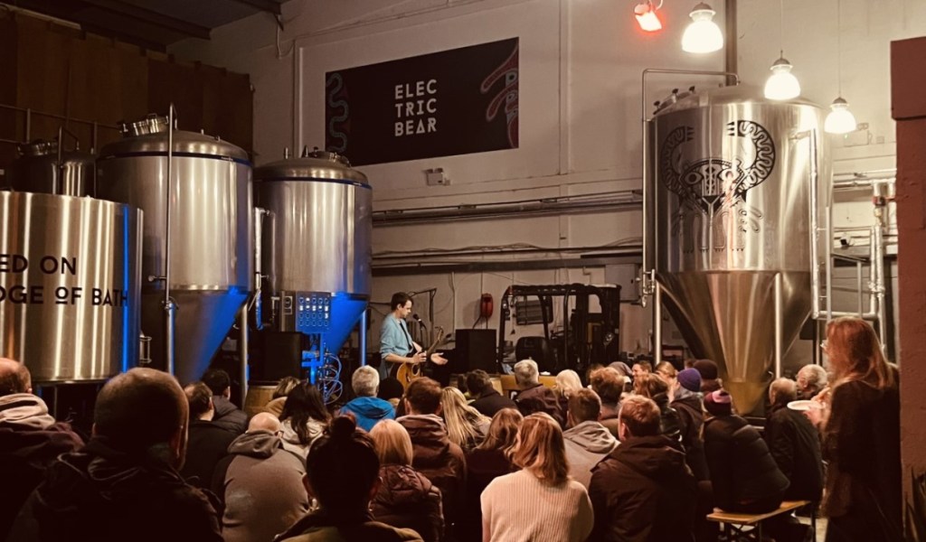 man playing guitar to audience in brewery