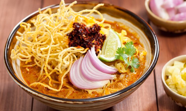 Thai curry sauce with slides red onion, a wedge of lime and crispy noodles on top